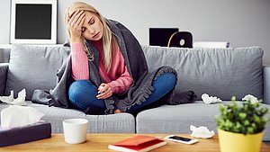 Hier sieht man eine erkältete Frau auf dem Sofa.