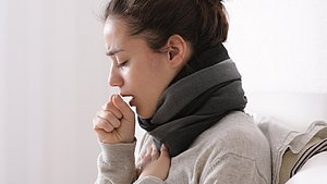 Eine erkältete Frau hustet in die Armbeuge.